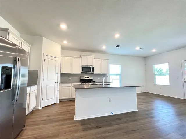 a kitchen with stainless steel appliances granite countertop white cabinets a refrigerator a sink a stove a microwave and wooden floors