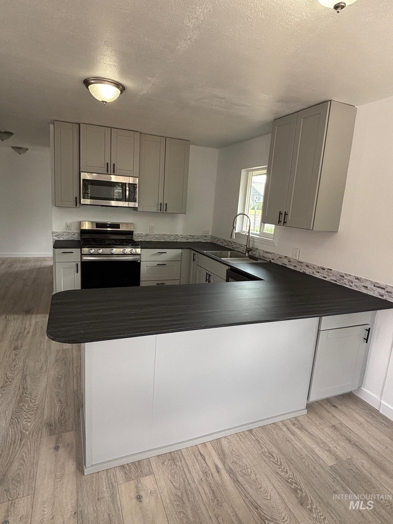 1203 Sycamore Street Clarkston, WA 99403 - Photo 6 of 31 Kitchen with appliances with stainless steel finishes, gray cabinets, a textured ceiling, light wood-style floors, and dark countertops
