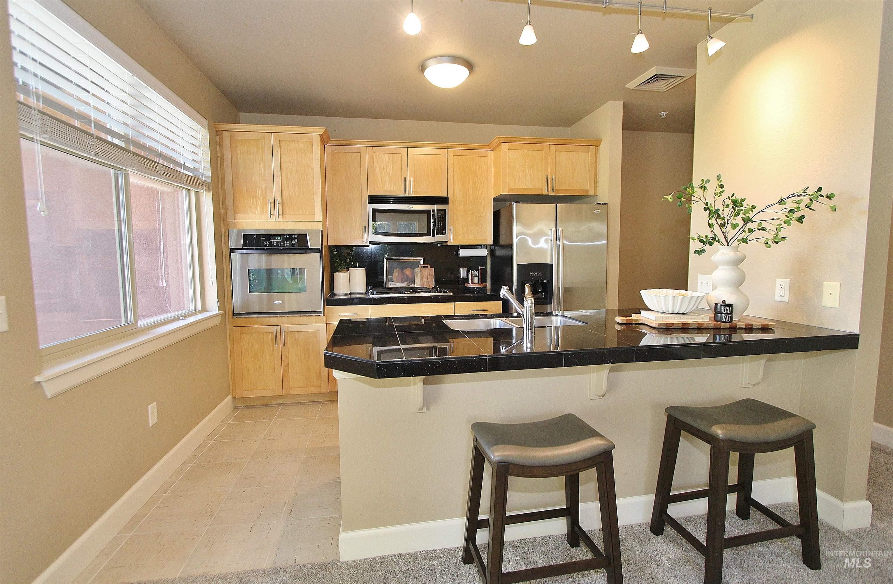 406 South 13th Street, Unit 303 Boise, ID 83702 - Photo 8 of 18 Kitchen featuring light wood finish cabinets, tile countertops, a peninsula, a breakfast bar area, and stainless steel appliances