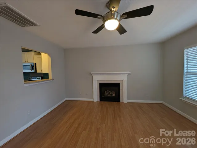 an empty room with wooden floor a chandelier fan and windows