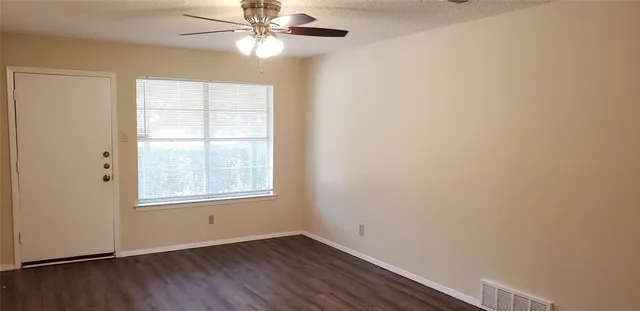 an empty room with wooden floor fan and windows