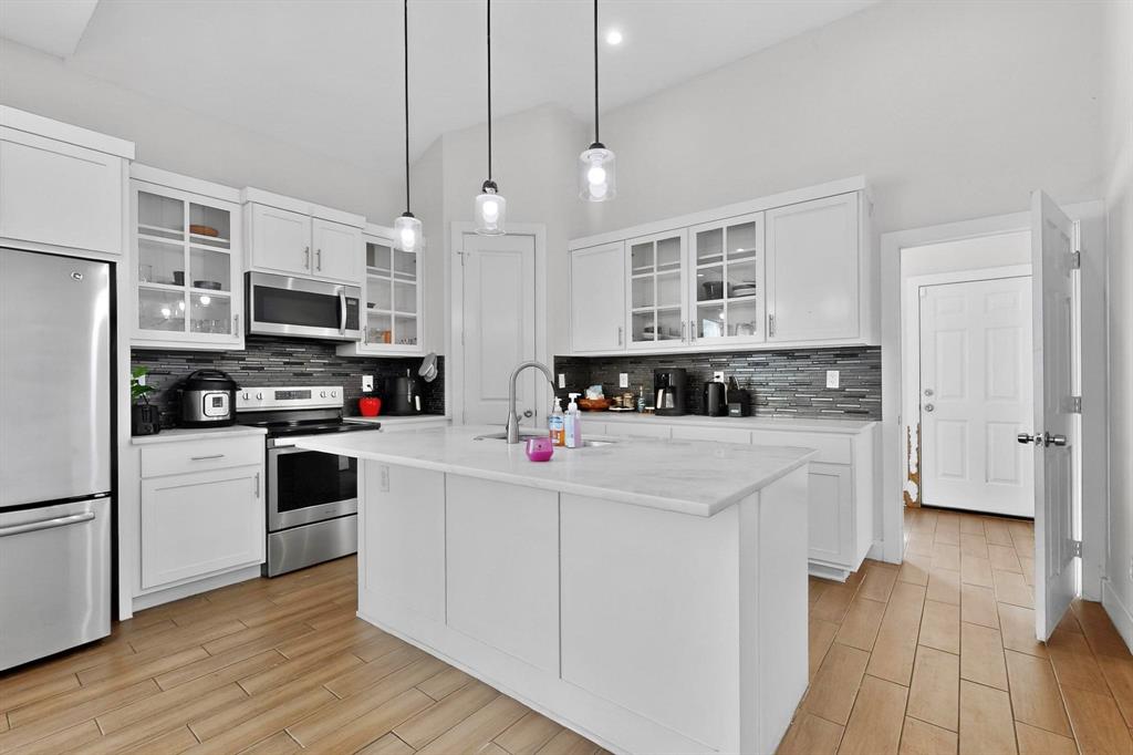 2015 Volga Avenue Dallas, TX 75216 - Photo 12 of 38 Kitchen with glass insert cabinets, stainless steel appliances, white cabinets, wood finish floors, and pendant lighting