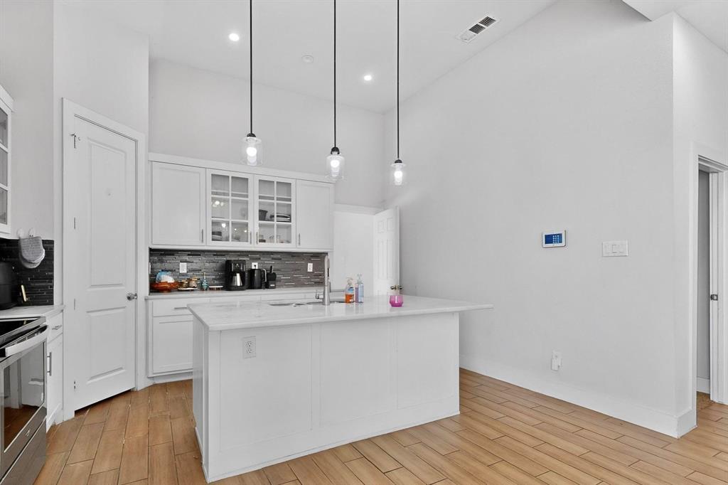 2015 Volga Avenue Dallas, TX 75216 - Photo 13 of 38 Kitchen featuring glass insert cabinets, wood tiled floors, decorative backsplash, white cabinetry, and vaulted ceiling