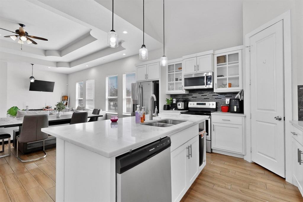 2015 Volga Avenue Dallas, TX 75216 - Photo 7 of 38 Kitchen with glass fronted cabinets, hanging light fixtures, stainless steel appliances, white cabinetry, and a kitchen island with sink