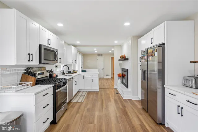 a open kitchen with stainless steel appliances granite countertop a refrigerator oven a sink dishwasher and white cabinets with wooden floor