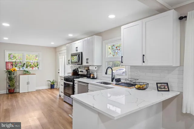 a kitchen with stainless steel appliances a stove a sink a refrigerator white cabinets and wooden floor