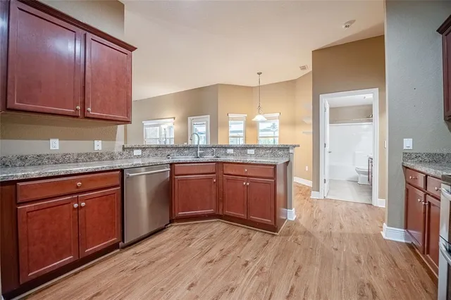 a kitchen with granite countertop wooden floors wooden cabinets a sink and dishwasher