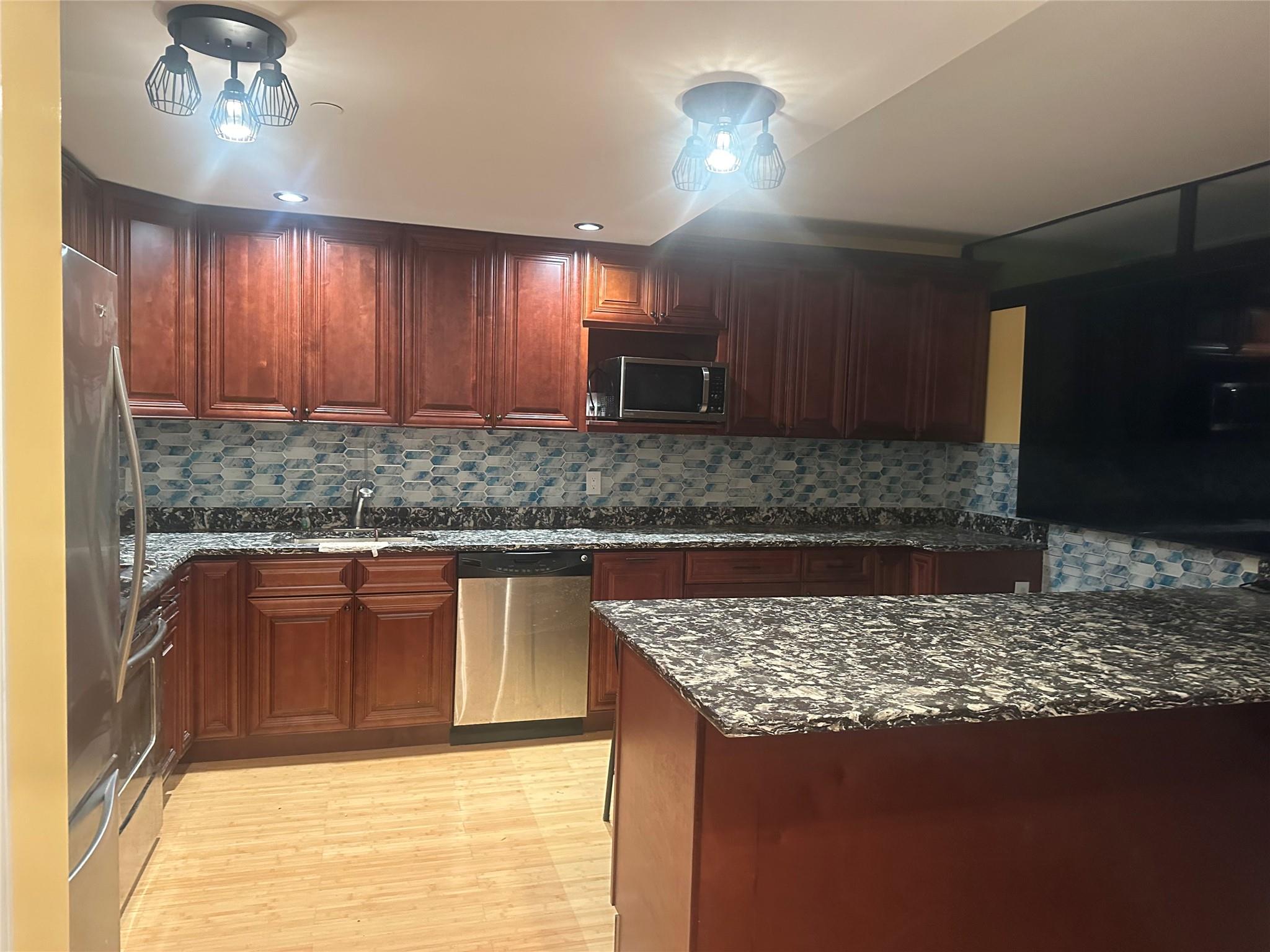 112-02 Northern Boulevard Queens, NY 11368 - Photo 2 of 11 Kitchen featuring stainless steel appliances, dark stone countertops, light wood-style floors, backsplash, and dark brown cabinets