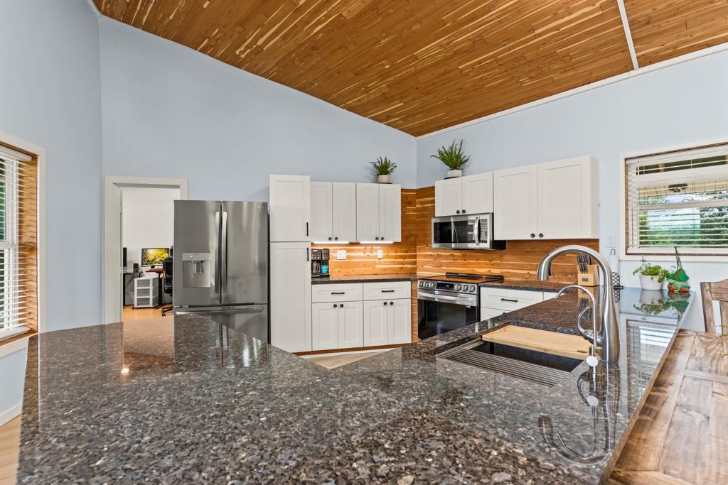 1129 Holly Road Gilmer, TX 75644 - Photo 7 of 31 Kitchen featuring a high vaulted wood-finish ceiling, dark speckled countertops, stainless steel appliances, white cabinetry, and a wood-finish backsplash