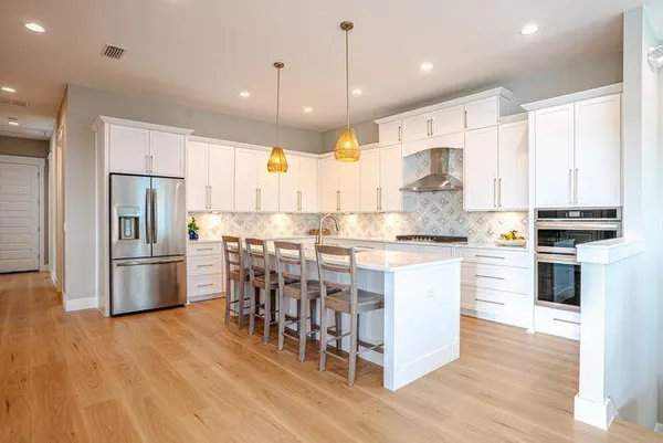 a kitchen with kitchen island granite countertop a refrigerator oven a sink and white cabinets with wooden floor