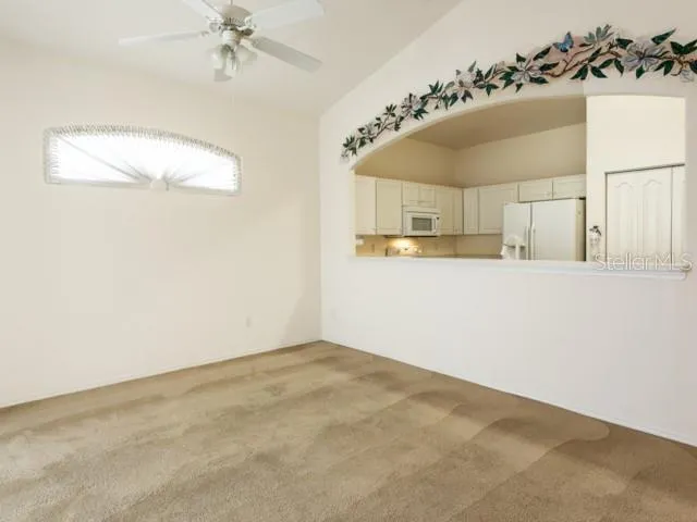 an empty room with a chandelier fan and kitchen view