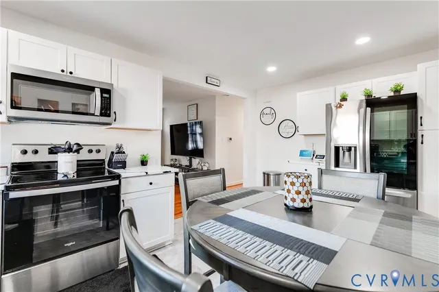 a living room with stainless steel appliances furniture a rug and a kitchen view