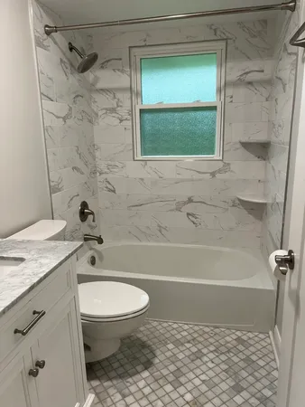 a bathroom with a granite countertop bathtub shower sink vanity and toilet