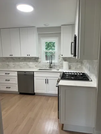 a white kitchen with granite countertop a stove top oven a sink and white cabinets with wooden floor