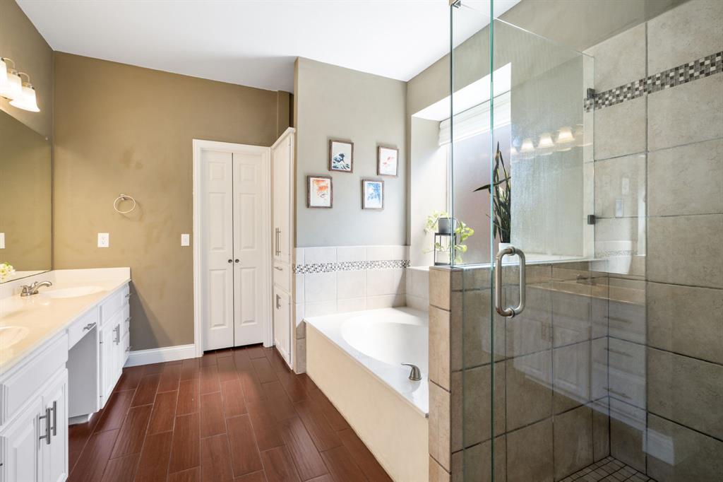 11414 Promenade Road Frisco, TX 75035 - Photo 12 of 24 Double vanity with white cabinetry, wood-finish flooring, built-in soaking tub, glass-enclosed shower, and a built-in linen cabinet