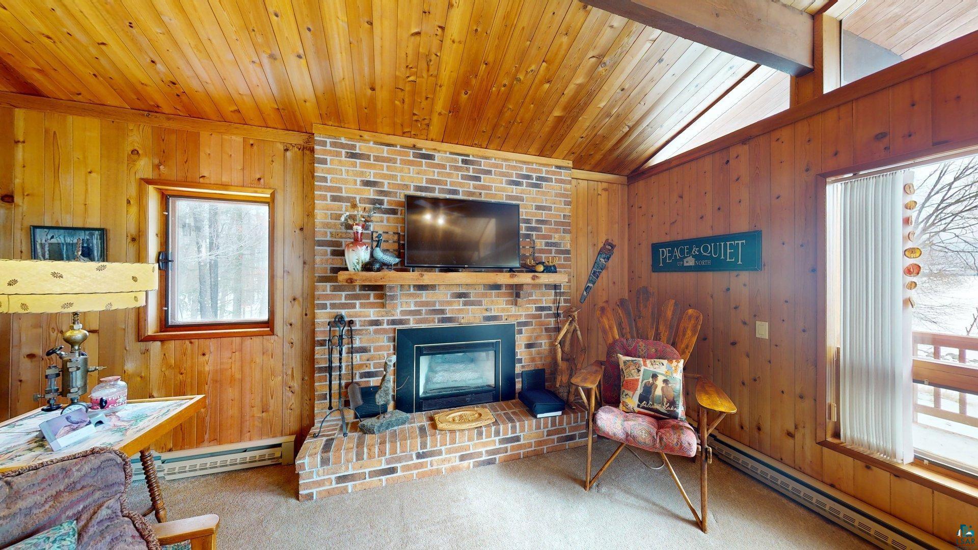 4512 Krollman Road Orr, MN 55771 - Photo 18 of 38 Carpeted living area featuring baseboard heating, wood ceiling, a fireplace, and lofted ceiling with beams