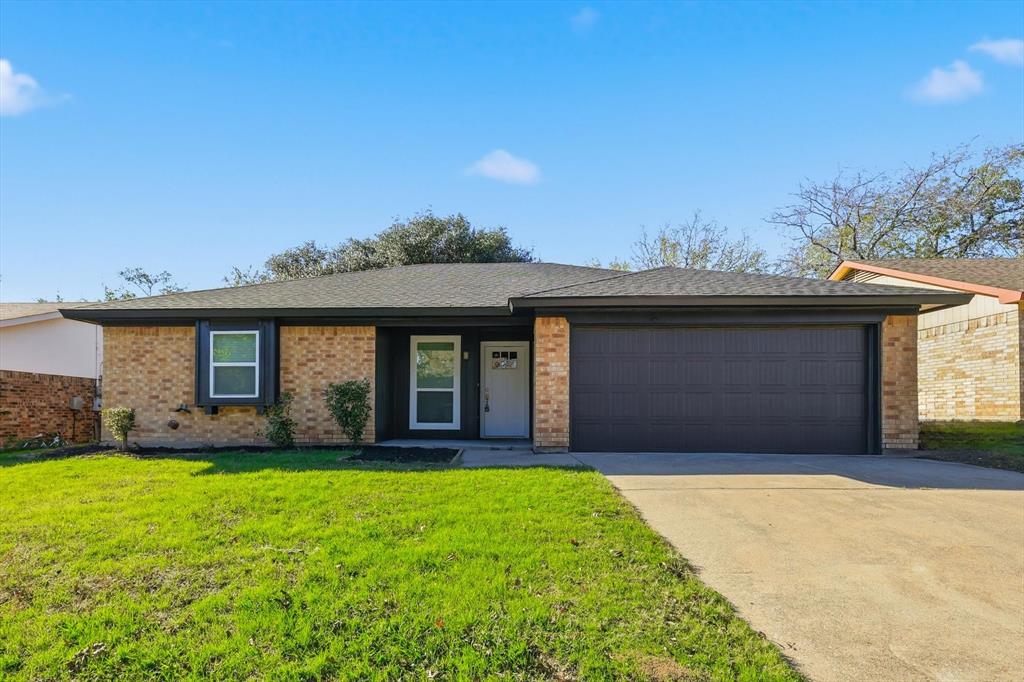Single story home featuring brick siding, concrete driveway, a front yard, an attached garage, and roof with shingles