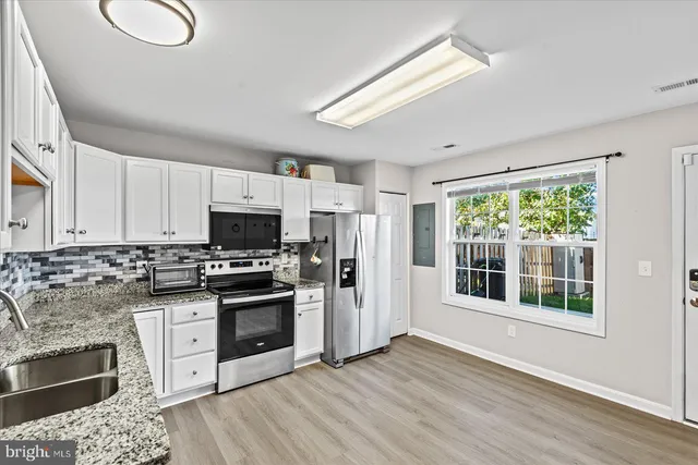 a kitchen with stainless steel appliances granite countertop a stove a sink dishwasher a refrigerator and a microwave oven with wooden floor