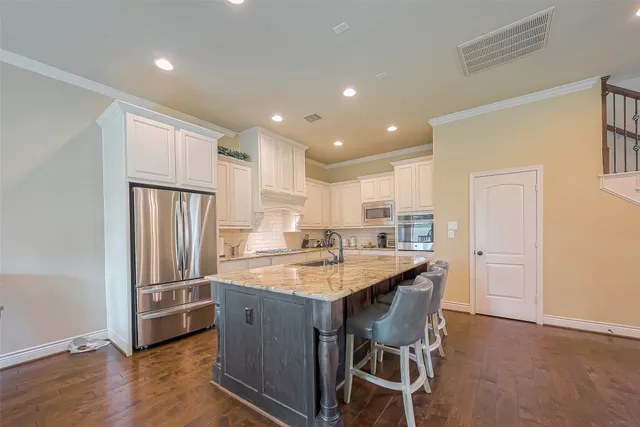 a kitchen with stainless steel appliances granite countertop a center island wooden floor and a refrigerator