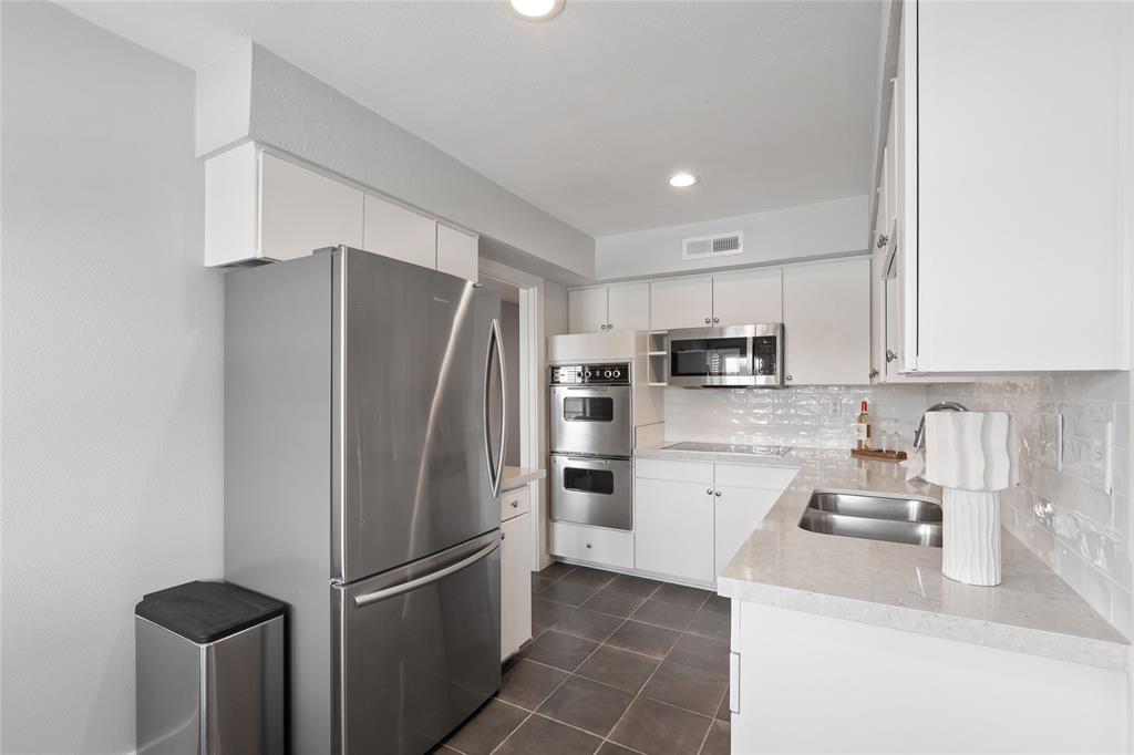 10727 Villager Road, Unit C Dallas, TX 75230 - Photo 16 of 39 Kitchen featuring appliances with stainless steel finishes, decorative backsplash, dark tile patterned floors, white cabinets, and light stone counters