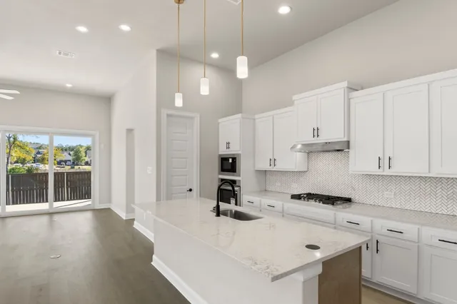 a kitchen with stainless steel appliances granite countertop a sink a stove a refrigerator and white cabinets with wooden floor