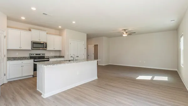 a kitchen with kitchen island granite countertop a stove top oven a sink and white cabinets with wooden floor