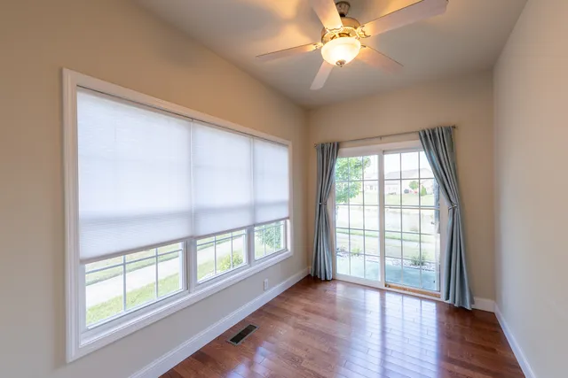 an empty room with wooden floor fan and windows