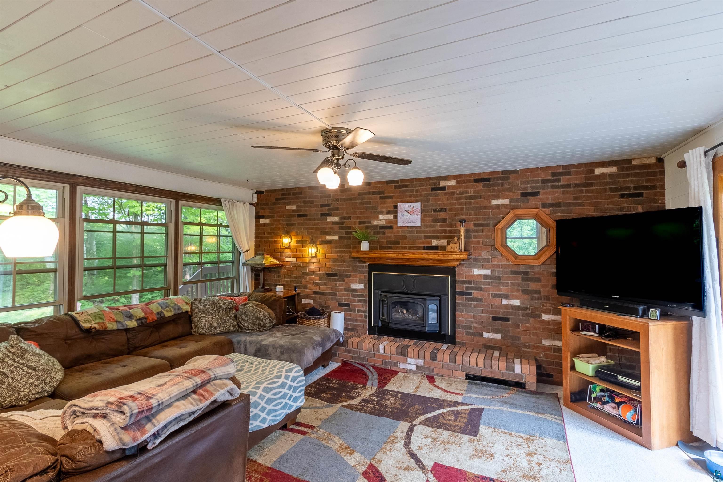 3976 Lavaque Road Hermantown, MN 55811 - Photo 8 of 38 Carpeted living room with brick wall, a fireplace, and ceiling fan