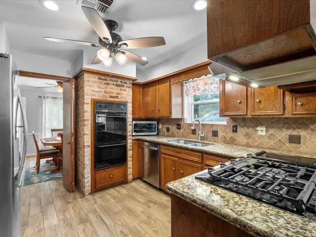 a kitchen with stainless steel appliances granite countertop a refrigerator a sink dishwasher a stove and white countertops with wooden floor