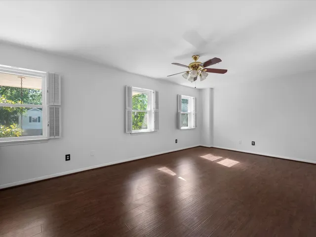 an empty room with wooden floor chandelier fan and windows