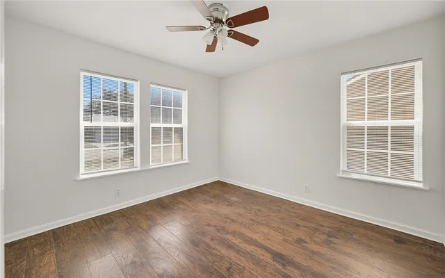 an empty room with wooden floor chandelier fan and windows