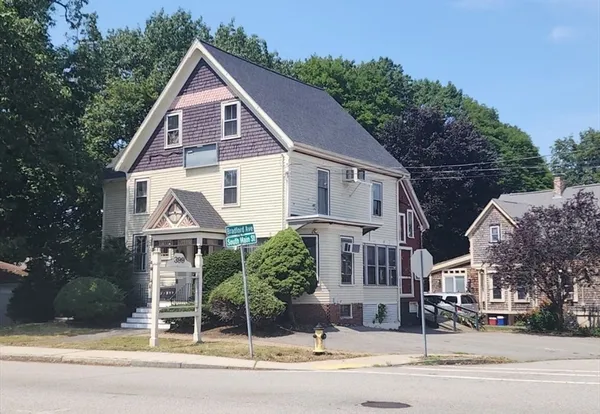 a view of a white house next to a road and trees