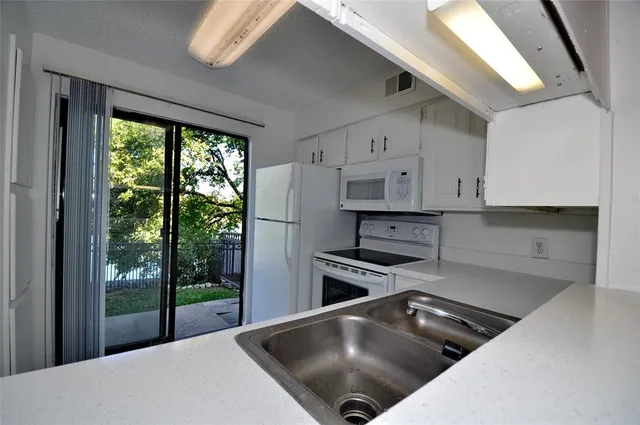 a kitchen with stainless steel appliances granite countertop a stove a refrigerator a sink and white cabinets with wooden floor