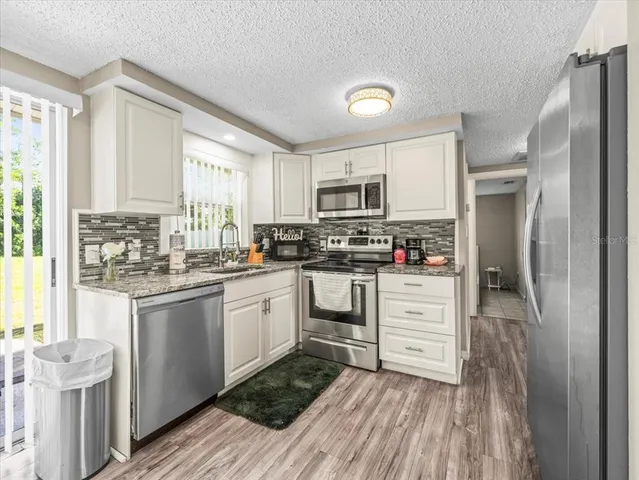 a kitchen with stainless steel appliances granite countertop a refrigerator a stove top oven a sink and dishwasher with wooden floor