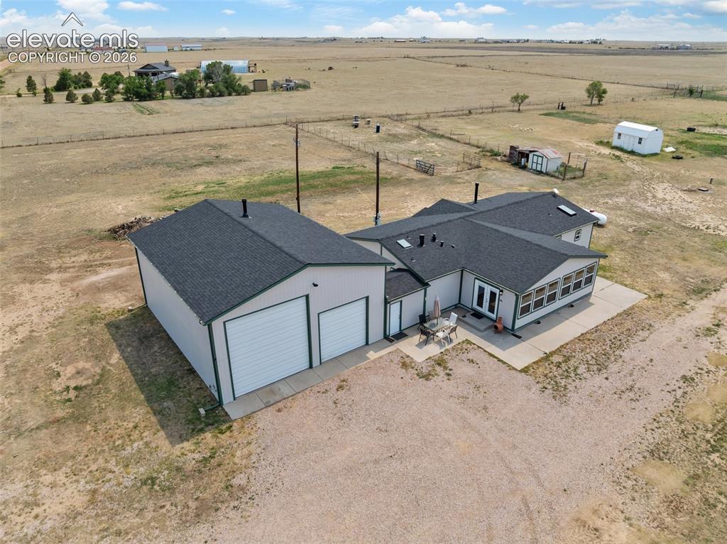 1350 South Calhan Highway Yoder, CO 80864 - Photo 5 of 45 Expansive property featuring a detached two-car garage with white overhead doors, a paved patio space, and a sunroom with multiple windows