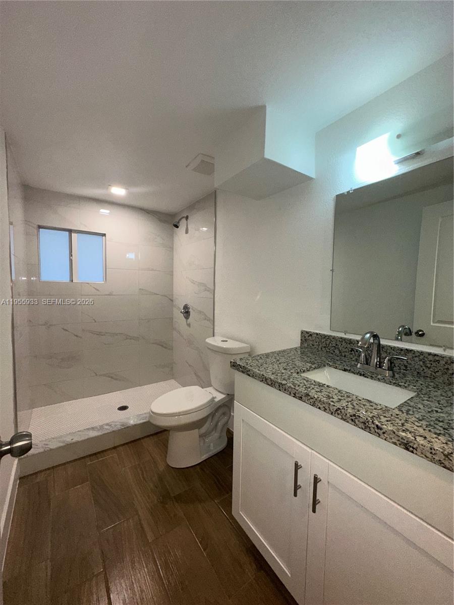3123 Northwest 22nd Court, Unit A Miami, FL 33142 - Photo 16 of 18 a bathroom with a granite countertop sink a toilet and a mirror