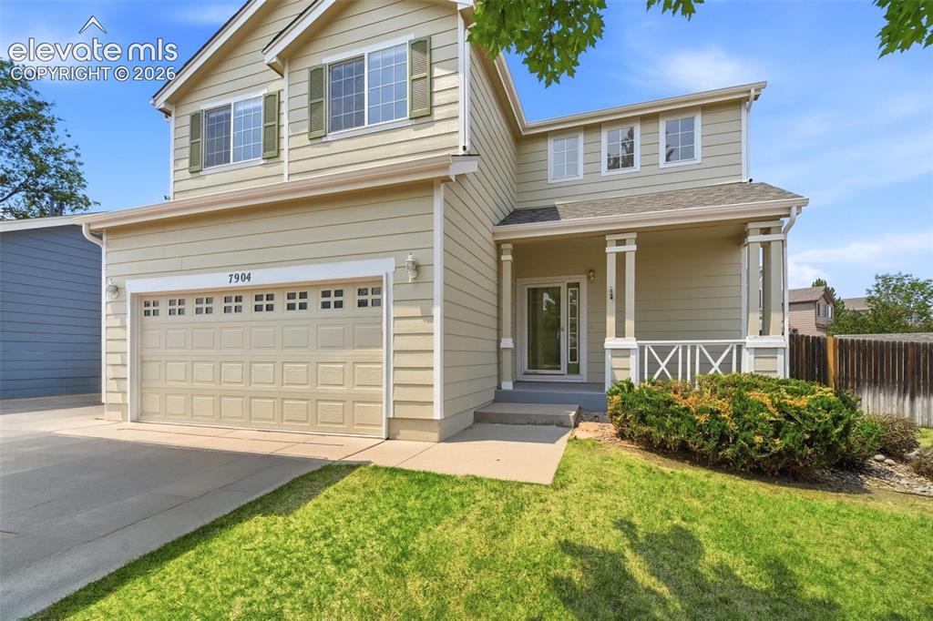 7904 Coffee Road Peyton, CO 80831 - Photo 2 of 48 Two-story residence featuring light-colored siding, a two-car garage with paneling and upper window inserts, and a covered front porch supported by columns