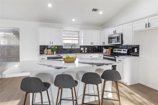 a kitchen with stainless steel appliances granite countertop a stove a sink a microwave a dining table and chairs with wooden floor