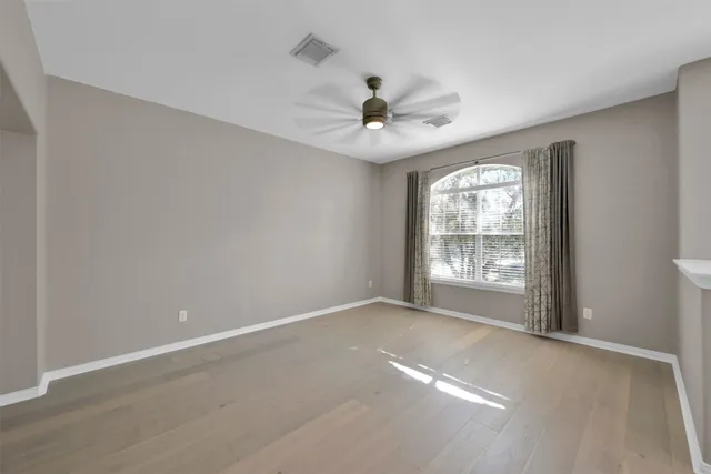 an empty room with chandelier fan and windows