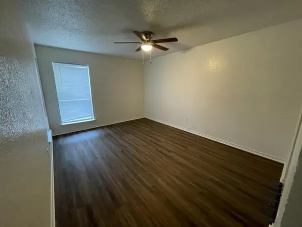 an empty room with wooden floor fan and windows