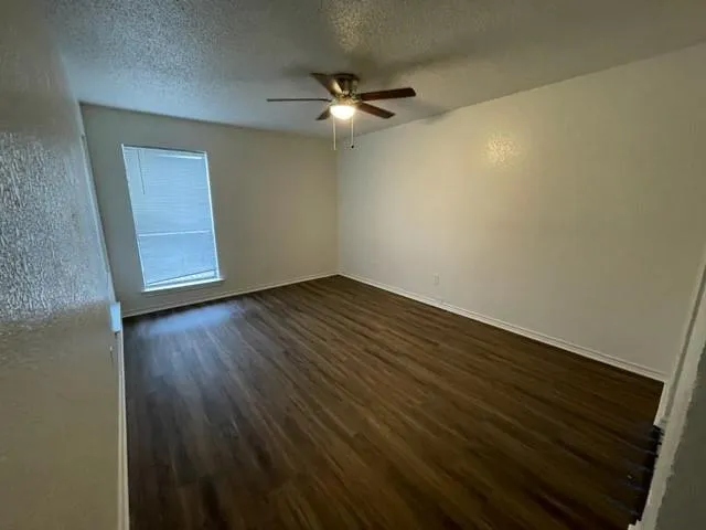 an empty room with wooden floor fan and windows