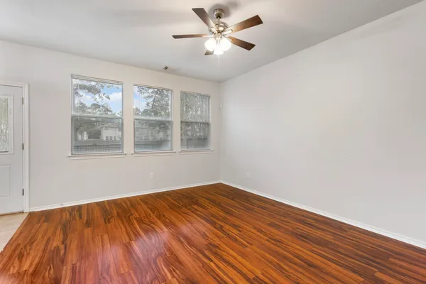 a view of an empty room with wooden floor and a ceiling fan