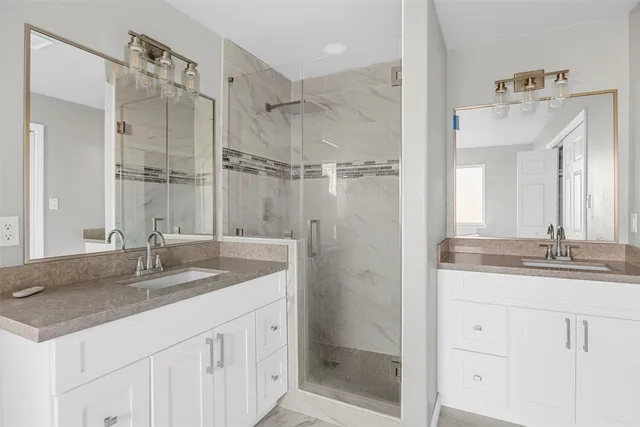 a bathroom with a granite countertop sink two mirror and shower