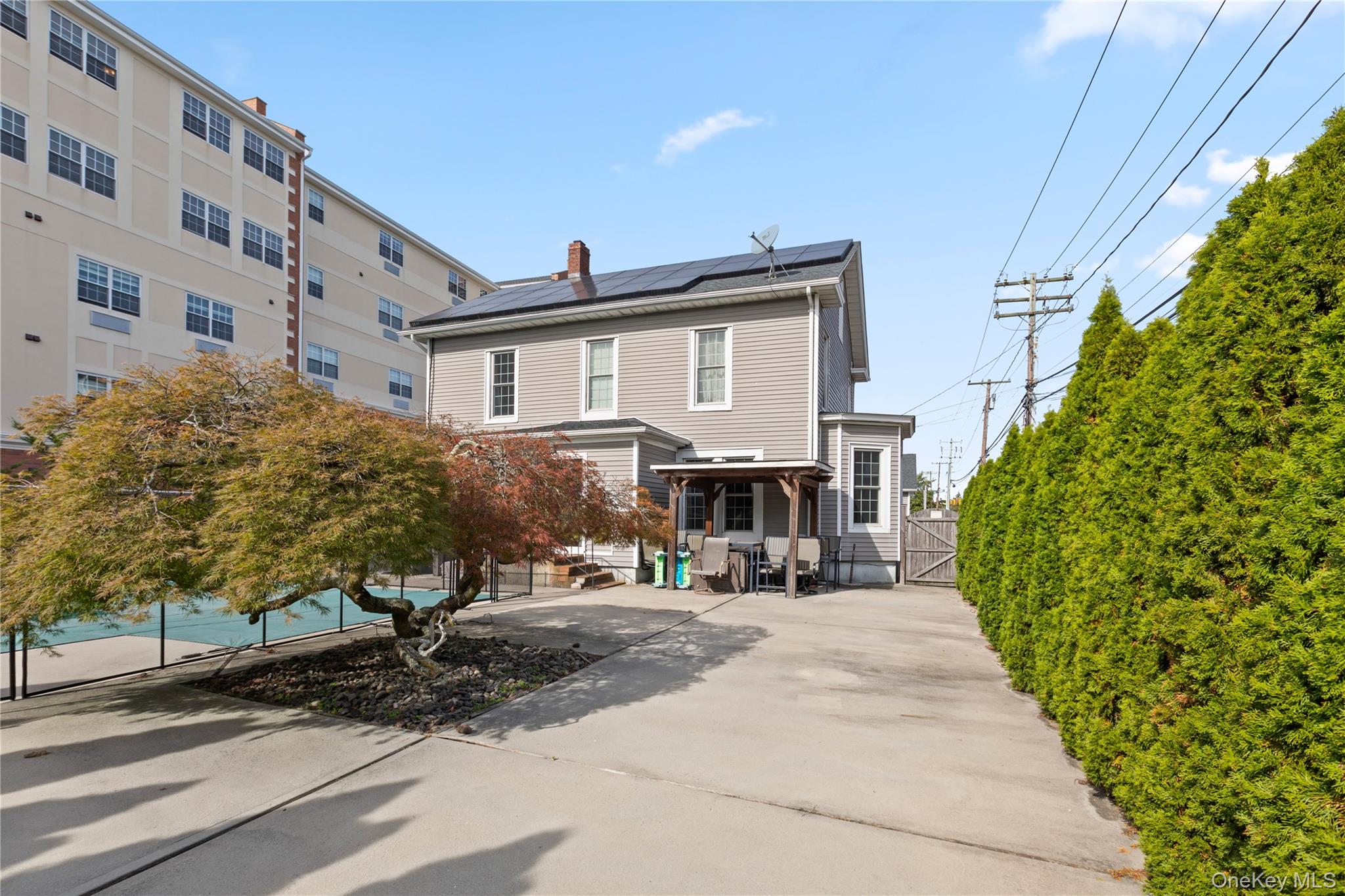 10 Maple Avenue Patchogue, NY 11772 - Photo 21 of 28 Rear view of house with a gate, solar panels, and a chimney
