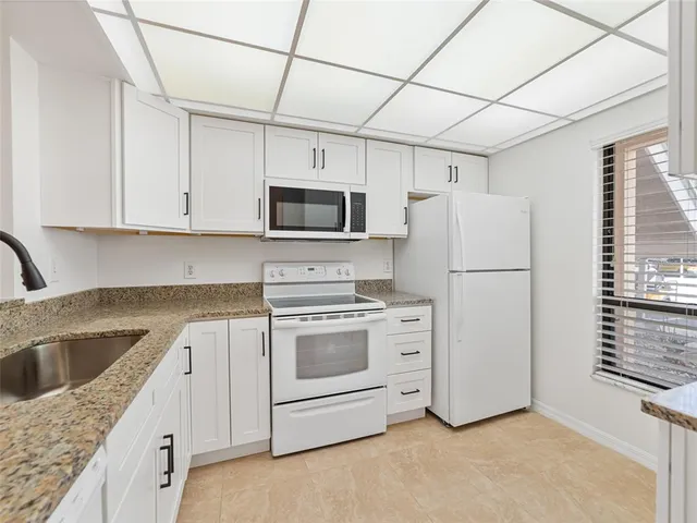 a kitchen with stainless steel appliances granite countertop a refrigerator a stove a sink dishwasher and white cabinets with wooden floor