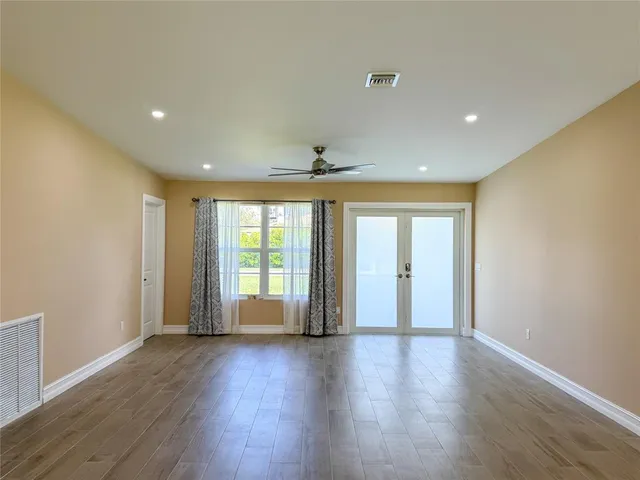 a view of an empty room with wooden floor and fan