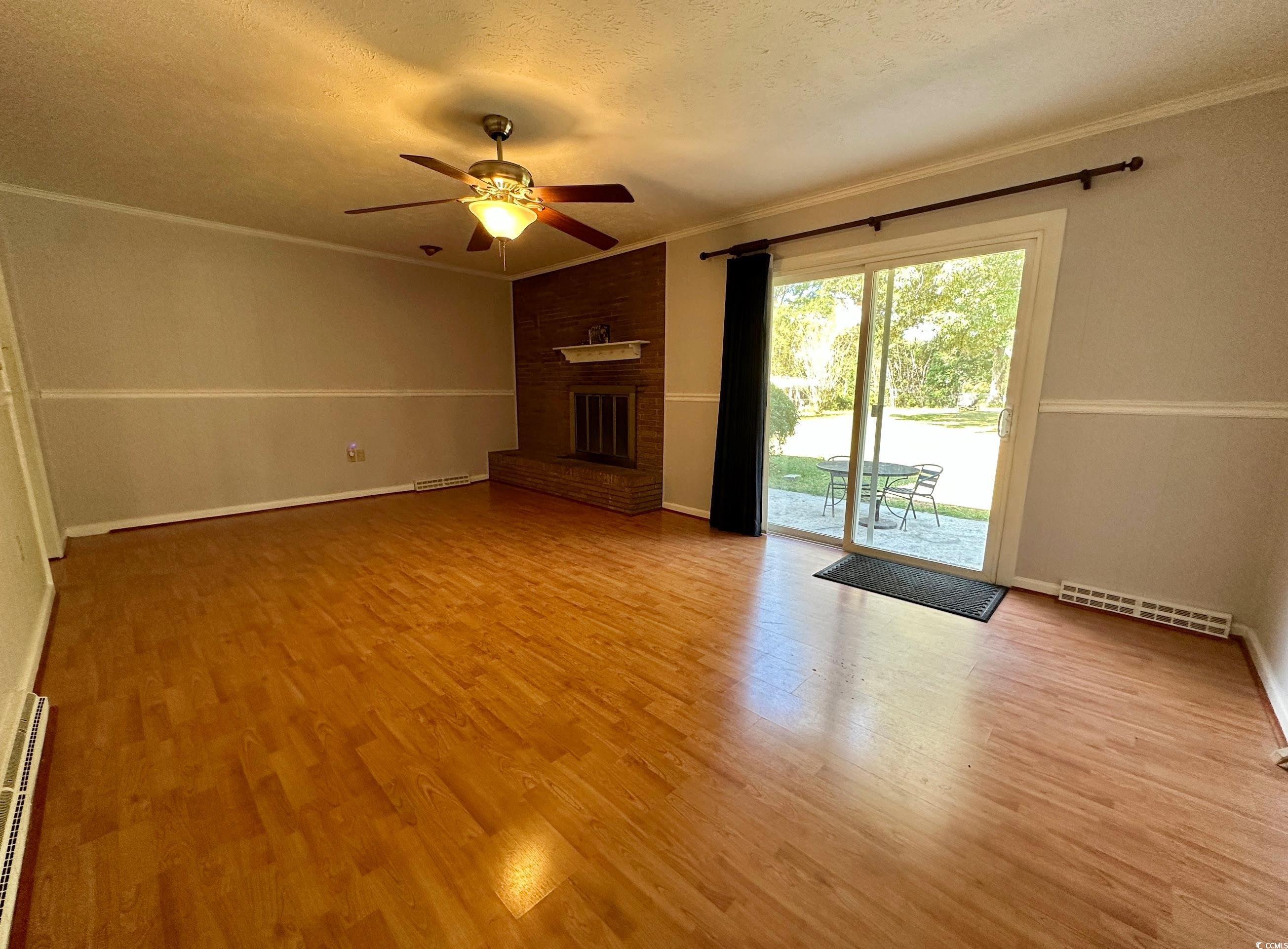 601 Jefferson Street Bennettsville, SC 29512 - Photo 17 of 20 Unfurnished living room featuring a textured ceiling, ornamental molding, light wood finished floors, a brick fireplace, and a ceiling fan