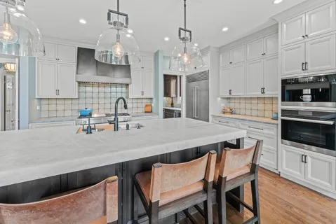a kitchen with stainless steel appliances a kitchen island hardwood floor sink stove and white cabinets