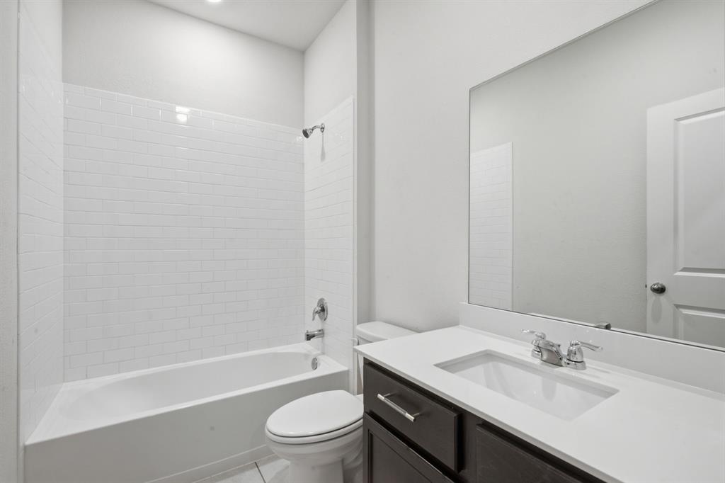 1328 Broaddus Road Forney, TX 75126 - Photo 22 of 31 Bathroom featuring a white subway tile tub surround, white bathtub, dark wood-finish vanity with a white countertop, and an integrated rectangular sink with chrome fixtures