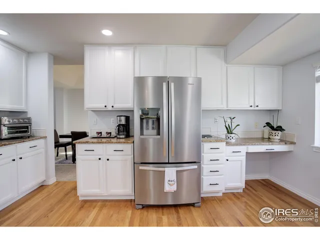 a kitchen with stainless steel appliances kitchen island granite countertop a refrigerator a stove a sink and white cabinets with wooden floor